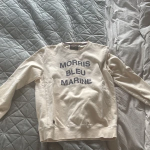 Vit sweatshirt från Morris - Säljer en stilren vit sweatshirt från Morris med texten 'Morris Bleu Marine' i blått på framsidan. Tröjan har långa ärmar och en klassisk rund halsringning. Perfekt för en avslappnad stil.