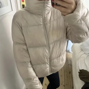 Trendig jacka  - Säljer en snygg vit dunjacka med hög krage och dragkedja. Jackan har en pufferdesign som ger en modern look och är perfekt för kyligare dagar. Den är långärmad och har en normal passform. Säljs för 1700 ny, säljs inte längre i butik 