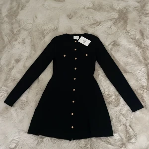 Svart klänning från H&M - Elegant svart klänning från H&M med långa ärmar och dekorativa knappar i guld. Perfekt för en stilren look, klänningen är helt ny med lappen kvar och säljs då jag har tappat bort kvittot.