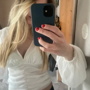 Vit blus med v-ringning - Säljer en stilren vit blus med v-ringning och långa ärmar. Blusen har en snygg rynkad detalj framtill som ger en elegant touch! 💝🥰