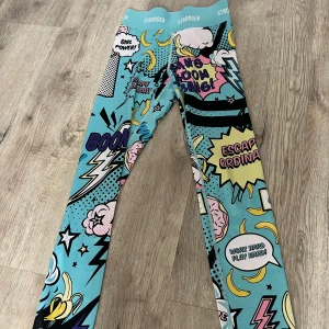 Färgglada leggings med serietidningsmönster från Stronger - Säljer ett par färgglada leggings från Stronger med ett coolt serietidningsmönster i blått, rosa, gult, svart lila och vitt. Perfekta för att sticka ut på gymmet eller vid andra aktiviteter. De har en hög midja för extra komfort och stöd. Super sköna och snygga!