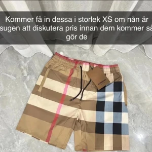 Rutig badshorts från Burberry - Jag har shortsen om max 2 veckor i storlek XS.                                                            Snygga  badshorts från Burberry med klassiskt rutigt mönster i beige, blått och rosa. Shortsen har en elastisk midja med snörning för justerbar passform. Perfekta för sommardagar vid stranden eller poolen.