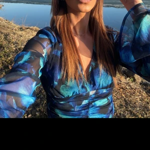 Blå blommig blus  - Snygg blå blus med blommigt mönster och långa ärmar. Perfekt för en somrig dag vid vattnet. Den har en v-ringad design som ger en elegant touch.