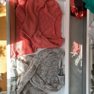 Rosa och grå stickade tröjor - Två stickade tröjor i olika färger. Den ena är rosa och den andra är grå med inslag av andra färger. 