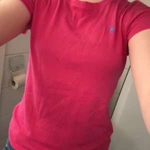 Rosa t-shirt från Ralph Lauren - Säljer en snygg rosa t-shirt från Ralph Lauren med det klassiska blå logotypen på bröstet. T-shirten har en normal passform och korta ärmar. 