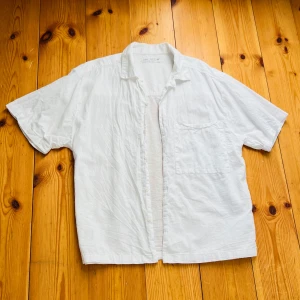 Vit kortärmad skjorta från Zara - Säljer en stilren vit kortärmad skjorta från Zara. Skjortan har en klassisk krage och knappar framtill. Perfekt för varma dagar med sin lätta och luftiga design.