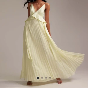 Ljusgul långklänning med volangdetalj - Elegant ljusgul långklänning med v-ringning och volangdetalj framtill. Klänningen har smala axelband och en öppen rygg med knytning. Perfekt för sommarens festligheter. ENBART testad 2-3 gånger och säljs pågrund av för liten i storleken för mig. Bilderna där klänningen testas är min mamma som är en storlek 38/40 mer 40 och hon säger den sitter lite tight över bysten och midjan, så någon med storlek 40 och lite större byst må uppleva den lite tightare. Köptes för 1569kr men säljs för 949kr 