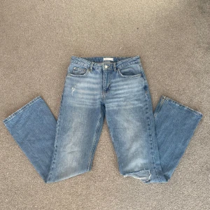 Blå jeans med hål  från gina tricot  - Snygga blå jeans med en avslappnad bootcut-stil och nice hål  på benen. De har en klassisk femficksdesign och en bekväm passform. Perfekta för en casual look!