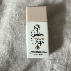 Golden Glow Drops från W7 - Golden Glow Drops från W7 är flytande bronzing drops som ger en strålande glöd. Förpackningen är vit med en praktisk pipett för enkel applicering. Perfekt för att skapa en solkysst look.