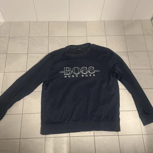 Blå sweatshirt från Hugo Boss - Snygg blå sweatshirt från Hugo Boss med deras ikoniska logga på bröstet. Tröjan har en slim fit passform och långa ärmar, perfekt för en stilren look. Den är tillverkad i ett mjukt material som ger en bekväm känsla hela dagen.