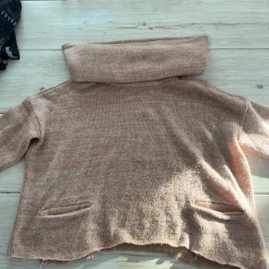 Ljusrosa stickad tröja, öppen vid axlarna  - Mysig ljusrosa stickad tröja med stor krage. Perfekt för kyliga dagar. Tröjan har en avslappnad passform och två diskreta fickor framtill.