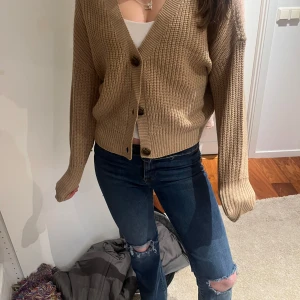 Beige stickad kofta - Säljer en mysig beige stickad kofta med knappar framtill. Koftan har en v-ringad design och långa ärmar, perfekt för kyligare dagar. Den är både stilren och bekväm, ett måste i garderoben!