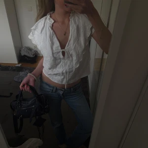 Vit blus med spetsdetaljer - Säljer en söt vit blus med spetsdetaljer, volanger och knytning framtill. Blusen har korta ärmar och en luftig passform, perfekt för varmare dagar. Den har en v-ringad design med fina volanger längs kanterna.Super söt blus från Zara storlek xs.  Gammal kollektion. Tröjan är verkligen super fin!! 