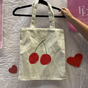 Beige shoppingväska med körsbärsmotiv - Vi är ett UF företag som säljer tygväskor med handmålade tryck på framsidan. Perfekt för att bära med sig det nödvändigaste med stil.
