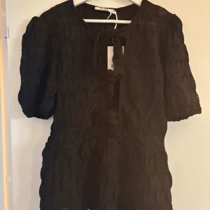 Svart puffärm topp med knytning - Snygg svart topp med puffärmar och knytning framtill från NAKD. Aldrig använd med lappar kvar. Säljer då jag inte hann returnera. 