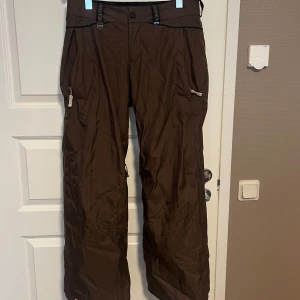 Bruna täckbyxor från Bonfire - Retro skidbyxor från Bonfire med broderad logga, herrstorlek L passar mig som normalt har storlek s-m. Lite oversize. Skulle säga att det är en unisexbyxxa.  Har endast använt dom fåtal gånger förra säsongen men köpta seconhand. 