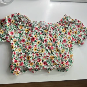 Blommig topp från Lindex - Säljer en söt blommig topp från Lindex i storlek 158/164. Toppen har korta ärmar och ett färgglatt blommönster i rosa, gul och grön. Perfekt för sommarens varma dagar! 🌸95kr+frakt pris kan diskuteras! Ha en bra dag😁!!