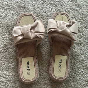 Beige sandaler från Joia - Snygga beige sandaler från Joia med en stor rosett på ovansidan. De har en fyrkantig tå och en bekväm sula, perfekta för varma dagar. Aldrig använda och därav prislappen kvar!