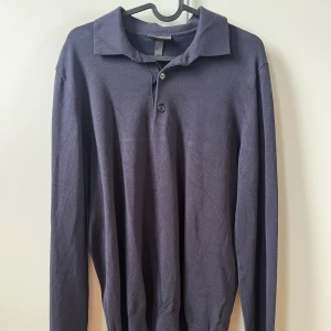 Mörkblå pikétröja från H&M - Säljer en stilren mörkblå pikétröja från H&M i slim fit. Tröjan har långa ärmar och knappar vid kragen. Perfekt för en avslappnad men ändå uppklädd look.