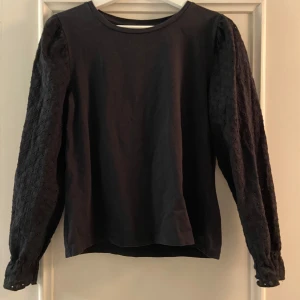 Svart långärmad topp från Pieces - Säljer en stilren svart topp från Pieces med långa ärmar i ett vackert spetsmönster. Perfekt för att ge en elegant touch till din outfit. Toppen har en rund halsringning och är tillverkad i ett mjukt material.