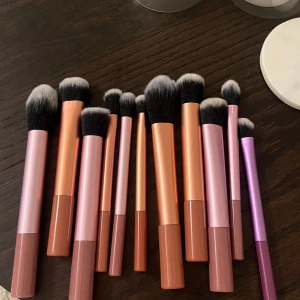 Set med sminkborstar i olika storlekar - Säljer ett set med sminkborstar i olika storlekar och former. Borstarna har handtag i metalliska nyanser av rosa och orange, med mjuka, täta borst i svart och vitt. Perfekt för applicering av foundation, rouge och ögonskugga. 11st helt osnvända