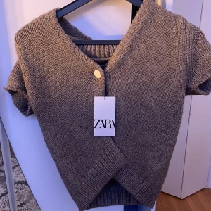 Beige  stickad kofta från Zara - Säljer en mysig grå stickad kofta från Zara med korta ärmar och en enkel knapp framtill. Perfekt för lager-på-lager-stil under kyligare dagar. Koftan har en klassisk design helt ny köpt för  330 men säljer för 230
