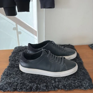 Blåa sneakers från Axel Arigato - Snygga blåa sneakers från Axel Arigato med vit sula och diskret logga på sidan. Skorna har en klassisk design med snörning och är tillverkade i skinn. Perfekta för en stilren look. Box och dustbag följer med 