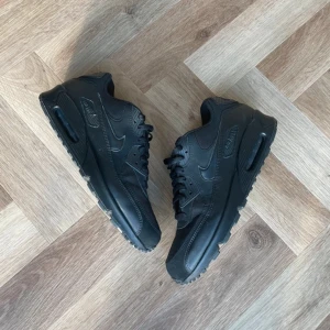 Svarta Nike Air Max sneakers - Snygga helsvarta Nike Air Max sneakers med klassisk design och synlig luftdämpning i sulan. Skorna har snörning och är tillverkade i syntetmaterial för en stilren look. Perfekta för en urban stil.