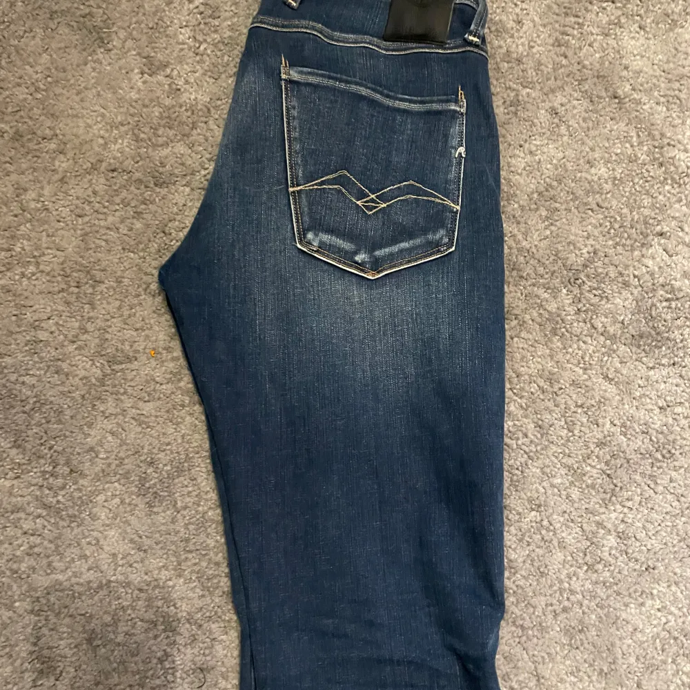 Snygga blå jeans från Replay, modell Anbass. De har en klassisk femficksdesign med en dragkedja och knapp framtill. Jeansen har en stilren look med diskreta sömmar och en liten logga på bakfickan. Storlek 29 32. Farkut & Housut.