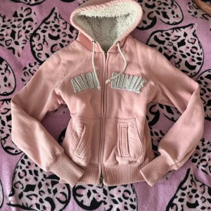Rosa hoodie från Abercrombie & Fitch - Mysig rosa hoodie från Abercrombie & Fitch med dragkedja och fodrad huva. Den har ribbade muddar och fickor framtill. (Står storlek L men passar som S)