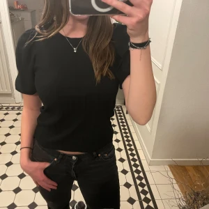 Svart ribbad topp - Snygg svart ribbad topp med korta puff ärmar och rund hals. Perfekt för en stilren look. Passar bra till både jeans och kjol.