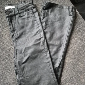 Svarta byxor från Vila - Snygga svarta byxor från Vila i en glansig finish. De har en klassisk femficksdesign och knappstängning fram. Perfekta för en stilren look.Stl XS