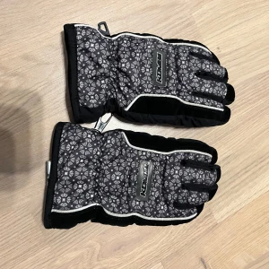 Svarta vinterhandskar från Kombi - Säljer ett par svarta vinterhandskar från Kombi med ett snyggt mönster i grått. Handskarna har förstärkta handflator och justerbara muddar för extra komfort. Perfekta för kalla dagar och håller händerna varma och torra. ❄️