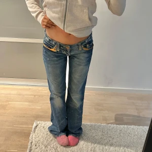 Blå bootcut jeans - Snygga blå bootcut jeans med låg midja och coola detaljer. Jeansen har en klassisk femficksdesign och slitna effekter för en trendig look. Perfekta för en avslappnad stil. Säljer då dom tyvärr är för stora 