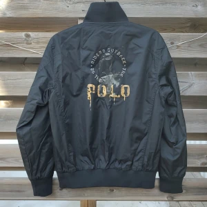 Svart bomberjacka från Ralph Lauren  - Säljer denna riktigt feta svarta bomberjacka från Ralph Lauren. Vändbar! Tre första bilderna visar ena sidan (blankt tyg), två sista andra sidan (mjukt tyg). Helsvart, ser ljusare ut på bild än i verkligheten. Märkt storlek L, sitter som en vuxen S. Superskick, sparsamt använd! Fråga gärna om mått etc. ✨