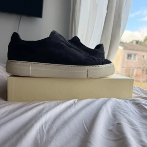 Arigato sneakers - Snygga svarta sneakers från Common Projects i mocka med en stilren design utan snörning. Skorna har en vit sula som ger en fräsch kontrast. Perfekta för en avslappnad men stilfull look.