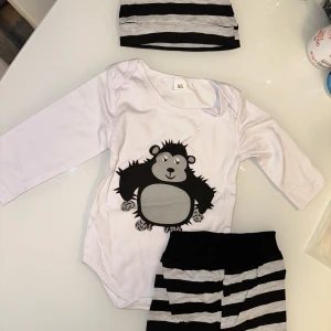 Vit och svart randig babyset med tryck - Säljer ett gulligt babyset med en vit långärmad body med ett tryck av en söt figur. Setet inkluderar även randiga byxor och en matchande mössa med öron. Perfekt för små äventyrare! 🖤🤍 från 1 år 🤗