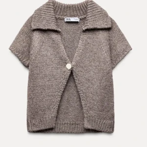 Beige stickad kofta från Zara - Säljer en mysig beige stickad kofta från Zara med korta ärmar och en stor knapp framtill. Västen har en ribbad krage och är perfekt för lager-på-lager-stil.
