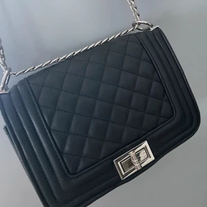 Svart quiltad axelväska med silver kedja från ur&penn - Snygg svart axelväska från ur & Penn köpt för 249kr men o ba använt 2 gånger. Den har quiltat mönster och silverfärgad kedja. Väskan har en stilren design med en praktisk dragkedja inuti för säker förvaring. Perfekt för att ge en elegant touch till din outfit.