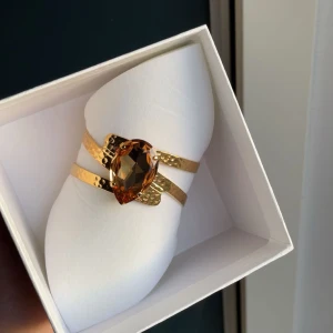 Guldarmband med stor brun sten (Intressekoll)  - Elegant guldarmband med en stor, facetterad brun sten i mitten. Armbandet har en unik design med två parallella band och en hamrad yta som ger en lyxig känsla. Perfekt för att ge en glamorös touch till din outfit. Nypris 1295 , passar alla storlekar då de är bändbart/justerbart, skriv gärna om ni har några frågor eller funderingar:) 🩷