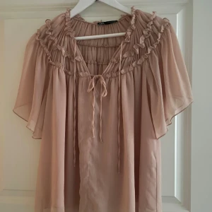 Rosa blus från Zara - Säljer en söt ros blus från Zara med volangdetaljer och knytning framtill. Blusen har korta ärmar och en luftig passform, perfekt för en stilren look.💕