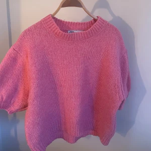 Rosa stickad tröja från Zara - Säljer en söt rosa stickad tröja från Zara. Den har en avslappnad passform med korta ärmar och ribbade kanter vid hals och nederkant. Perfekt för en mysig dag! 💖
