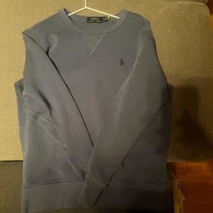  sweatshirt  Polo Ralph Lauren - Snygg blå sweatshirt från Polo Ralph Lauren med klassisk rund hals och diskret broderad logga på bröstet. Tröjan har långa ärmar och är tillverkad i mjuk bomull, perfekt för en chill och stilren look.