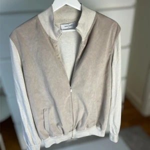 Beige mockajacka från Gran Sasso - Snygg beige jacka från Gran Sasso med mjuk mockakänsla framtill och ribbad krage. Jackan har dragkedja, fickor och är i en ljus, stilren färg. Perfekt för dig som gillar en clean och modern look. Storlek 52, passar som M/L