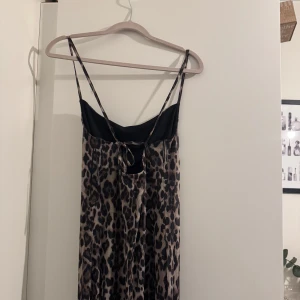 Leopardmönstrad långklänning  - Supersnygg långklänning från Gina tricot med leopardmönster i beige och svart. Klänningen har tunna axelband, smickrande passform och snygg snörning i ryggen. Perfekt för dig som vill sticka ut med en trendig look.