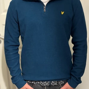 Blå half zip tröja från Lyle & Scott - Snygg blå långärmad tröja från Lyle & Scott med half zip dragkedja. Tröjan är i en lite grönare nyans än vad som syns på bilden. Tröjan är inte mycket använd och därav finns priset.
