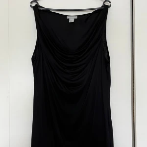 H&M svart topp, storlek L - Ärmlös svart topp med drapering framtill från H&M i storlek L. 100% viskos.  Nyskick.   Mått: Längd ca 77 cm Byst ca 55 cm Midja ca 50 cm Axel till axel ca 34 cm