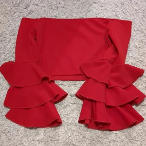 Röd croppad topp med volangärmar - Säljer en riktigt snygg röd croppad topp med långa ärmar och stora volanger längst ner på ärmarna. Toppen har en offshoulder-design som ger en trendig vibe och är perfekt för dig som vill sticka ut. Materialet känns mjukt och följsamt.