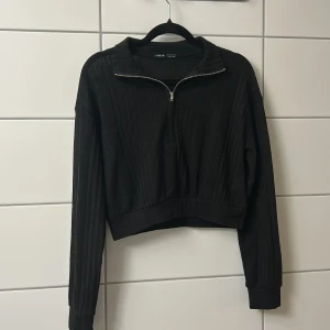 Svart ribbad half zip tröja Shein - Svart ribbad tröja från Shein med half zip-dragkedja och hög krage. Croppad modell med långa ärmar och relaxed fit. Perfekt för dig som gillar en stilren och enkel look med lite edge.