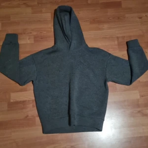 Mörkgrå hoodie i storlek S - En basic mörkgrå hoodie med huva och långa ärmar. Tröjan har en klassisk passform och är tillverkad i mjukt material som passar perfekt för chill dagar. Enkel och stilren design utan tryck eller mönster.